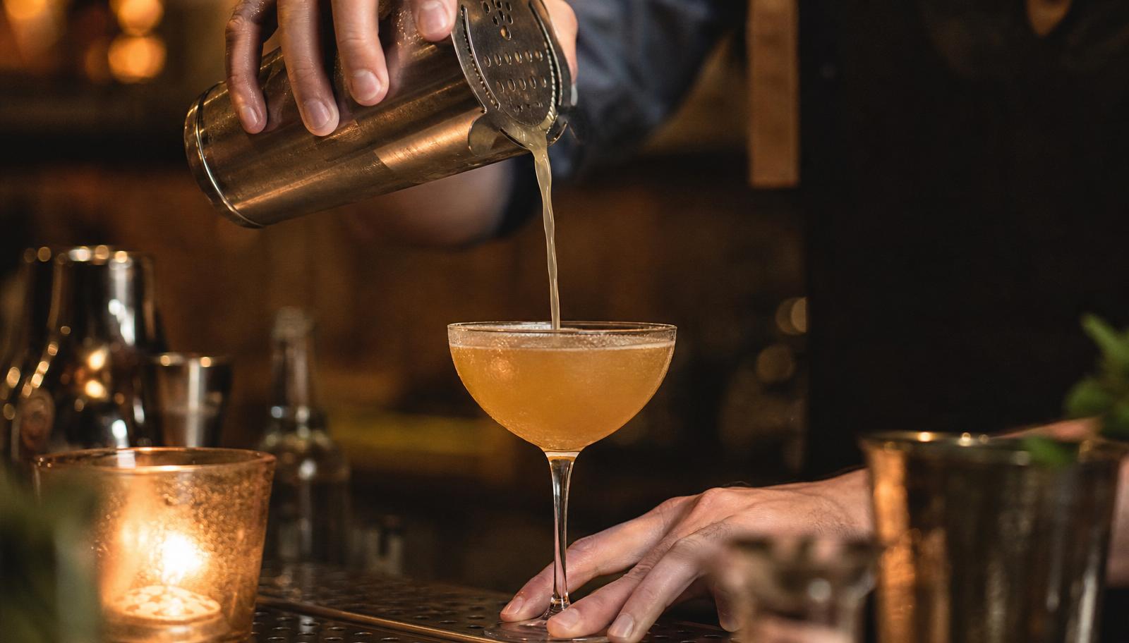 Bartender pouring a cocktail into a crystal coupe